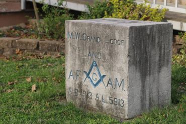 Stone block with Masonic emblem and inscription in grass.