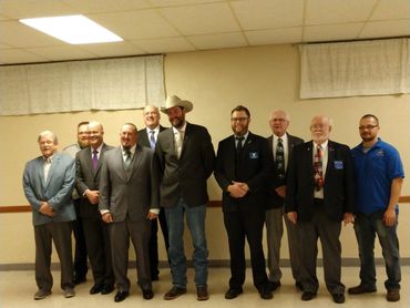 A group of eleven men posing indoors, dressed formally and casually.