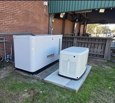Two white Generac generators installed outside a brick building.
