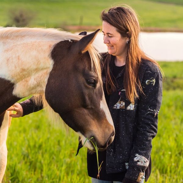 A woman smiling while petting a horse in a green field.