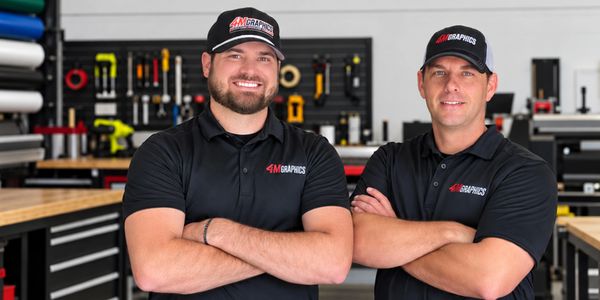 Two men in branded work shirts and caps in a workshop.