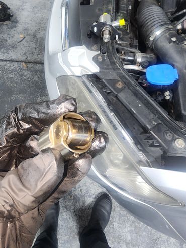 Gloved hand holding a car part near the engine.