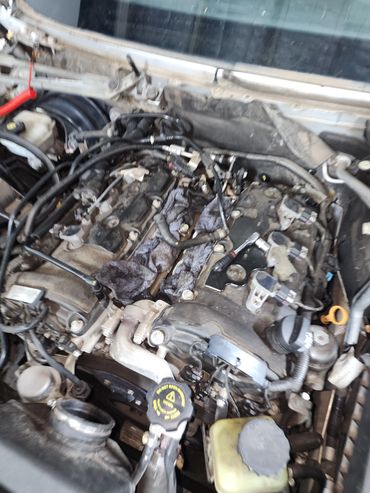 Close-up of a car engine with parts exposed and dirty rags.