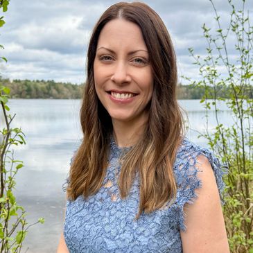 Smiling woman in blue lace dress by a lakeside with greenery around.