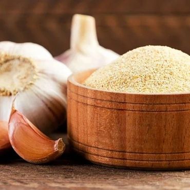 Garlic bulbs and garlic powder in a wooden bowl on a rustic surface.