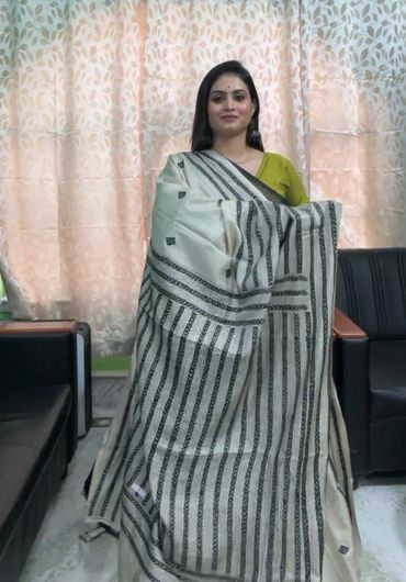 Woman draped in a black and white striped saree with a green blouse indoors.