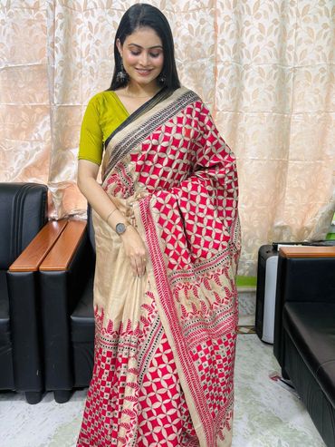 Woman smiling in a vibrant red and beige saree with a green blouse indoors.
