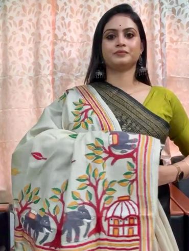 Woman showcasing a white saree with colorful elephant and tree motifs.