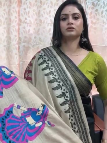 Woman showcasing a beige saree with vibrant blue and pink traditional dance motifs.
