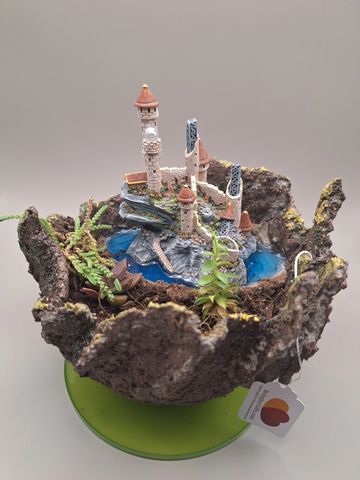 A miniature castle and moat scene inside a rustic bowl with small plants.