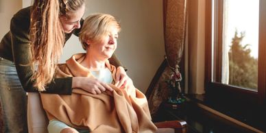 A woman giving a blanket to another woman sitting on a chair