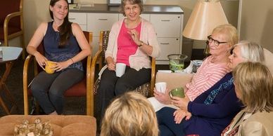 A young woman and elderly women sitting on chairs and a couch, talking