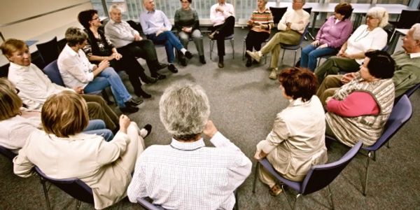 A large group of elderly people sitting on chairs, forming a circle