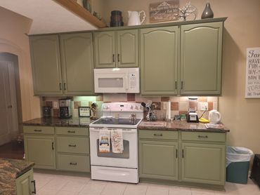 Cozy kitchen with green cabinets and white appliances.