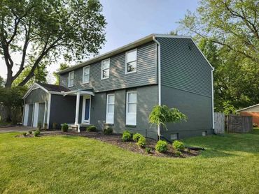 A two-story gray house with a well-maintained lawn and shrubs.