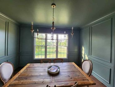 Rustic dining room with wooden table and elegant chairs under a chandelier.