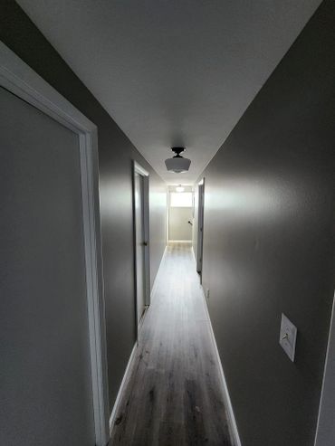 A narrow, minimalist hallway with gray walls and wood flooring.