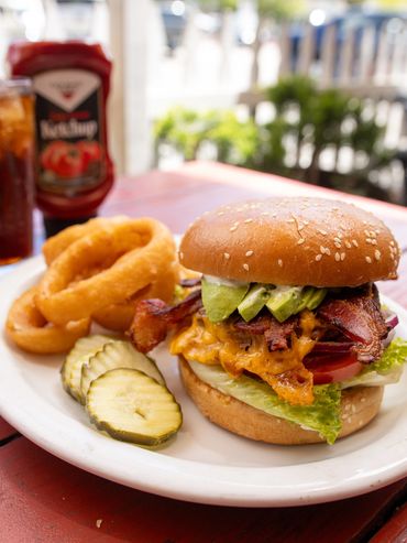 Large bacon cheeseburger with avocado, side of pickles and onion rings