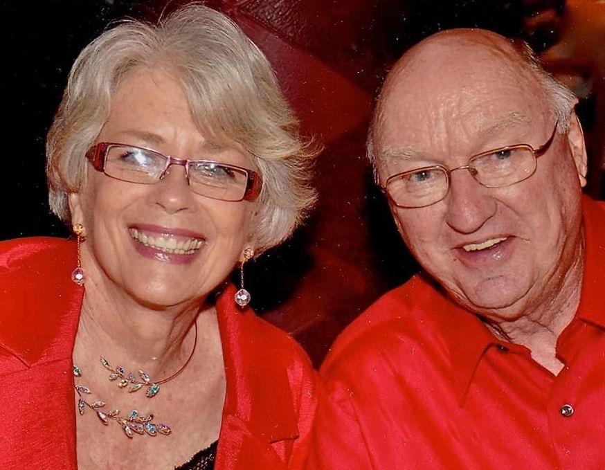 Smiling elderly couple wearing red clothing and glasses.