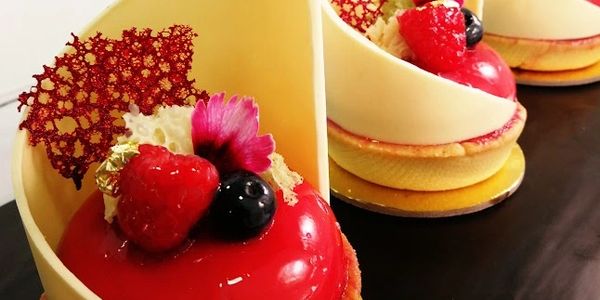 Elegant red berry mousse cakes with white chocolate decor and edible flowers.
