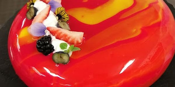 A glossy red and yellow glazed cake decorated with berries and edible flowers. This and more is what is teaching in the patisserie classes
