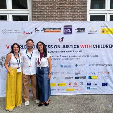 Three people smiling in front of a banner at a justice conference for children in Madrid.