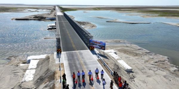 A newly constructed bridge over a wide river with people standing at its entrance.