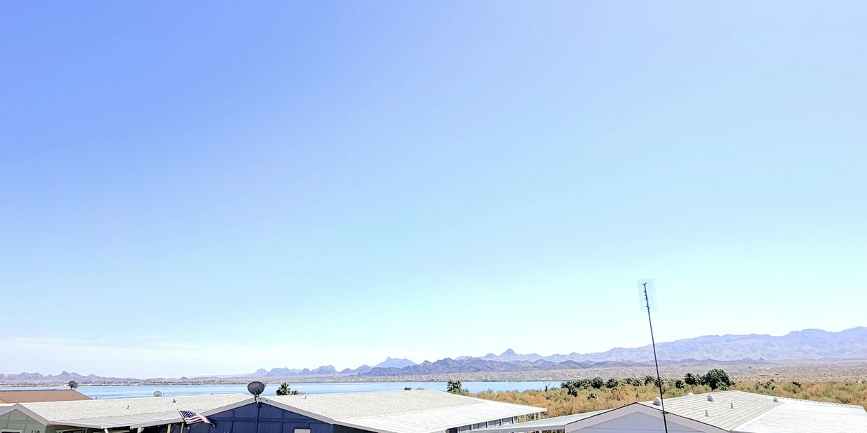 Clear blue sky over lakeside houses with mountains in the distance.