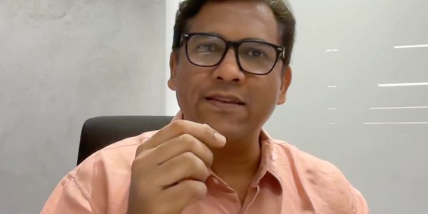 Man in glasses and peach shirt speaking in an office setting.