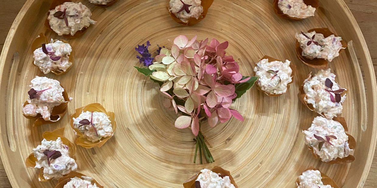 Appetizers with creamy salad in crispy cups on a bamboo tray with flowers.