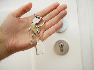 Hand holding house keys in front of a door lock.