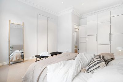 Bright, minimalist bedroom with white walls, bed, and large mirror.