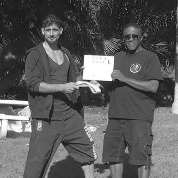 Two men outdoors, one holding a sign and the other holding a snake.