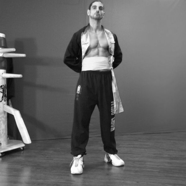 Man in martial arts attire posing confidently in a training space.