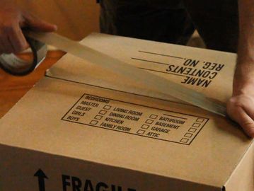 Professional packer sealing a moving box labeled 'Fragile' with packing tape.
