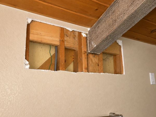Structural remodeling work in progress showing a wall opening cut between living spaces, exposed fra
