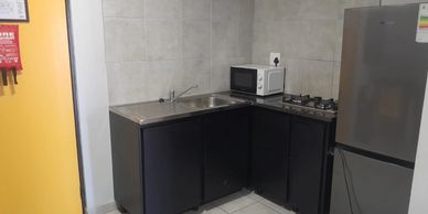Compact kitchen with black cabinets, sink, microwave, stove, and fridge.