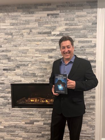 Man in suit holding the book 'Two Connected Souls' by Bruce K. Royer.