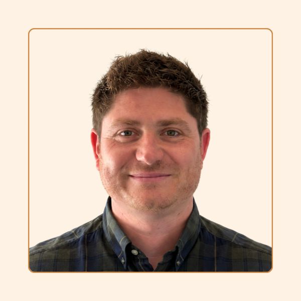 Smiling man with short brown hair and a checkered shirt.