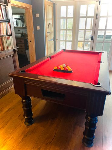 A red-felt pool table with balls arranged in a triangle in a cozy room.