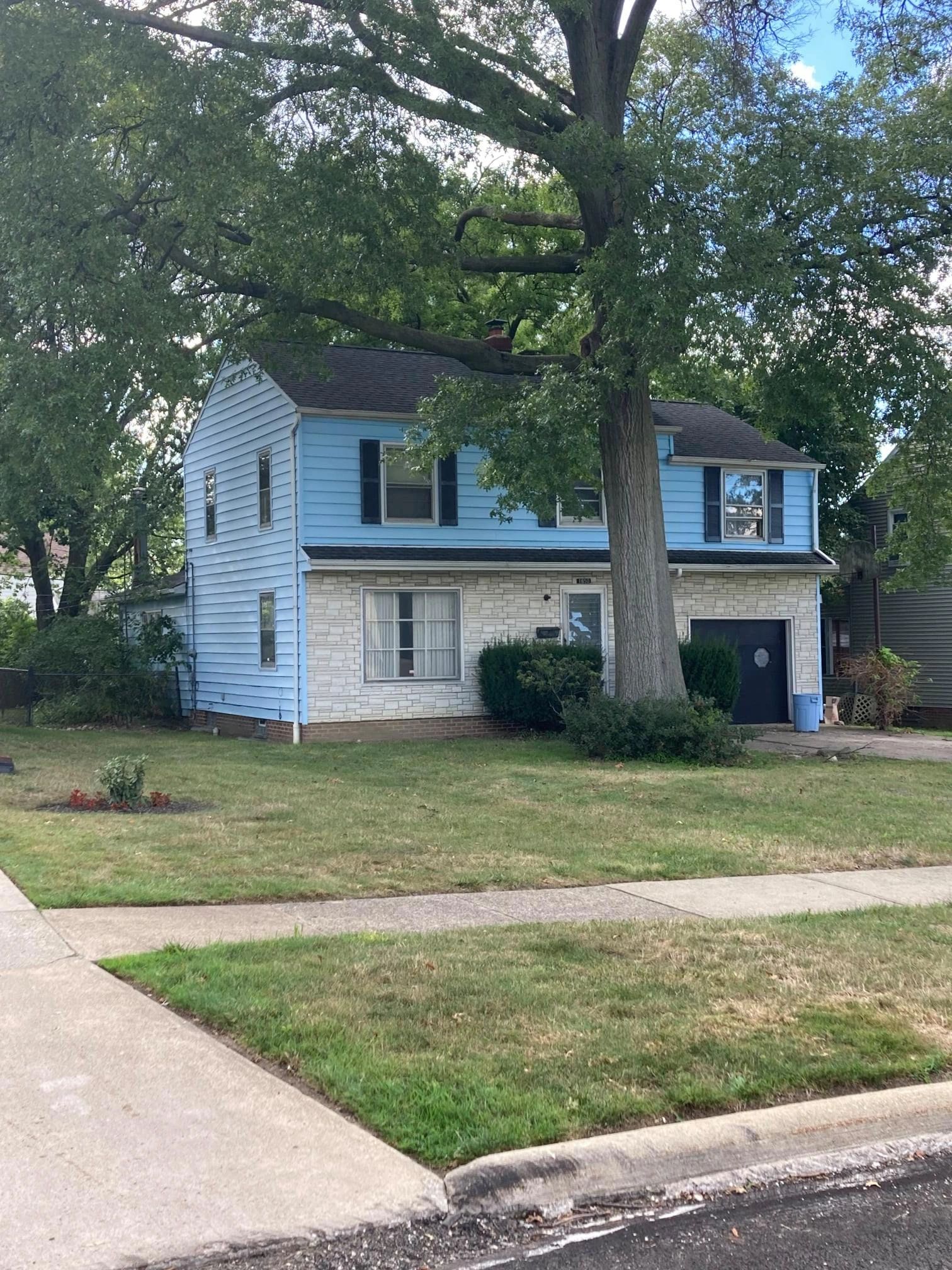 Blue two-story house with large tree in front.