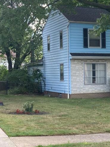 Blue two-story house with large tree in front.