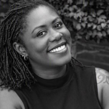 Smiling woman with dreadlocks in black and white photo.
