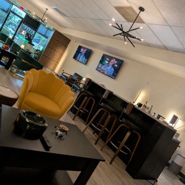 Modern lounge area with yellow chair, bar stools, and two TVs on the wall.