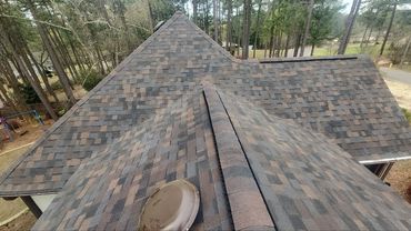 A newly shingled roof on a house surrounded by trees.