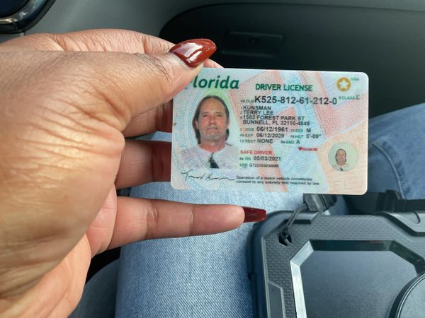 Hand holding a Florida driver's license with red nails.