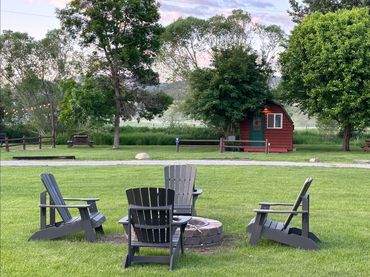 Adirondack chairs around fire pit on the grass near camper cabin