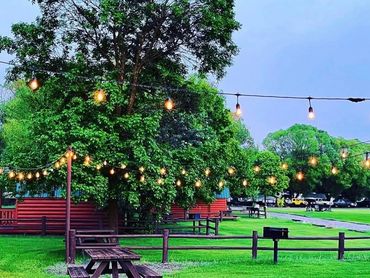 Party lights over picnic tables and bbq with lush green grass