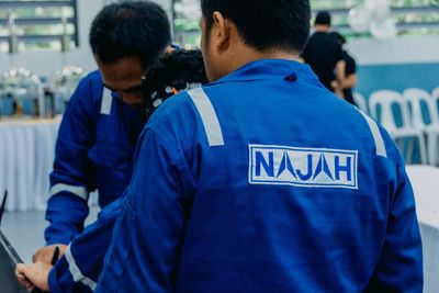 Personnel wearing a blue coverall with NAJAH Industries OPC logo on back. NAJAH means “success” in A