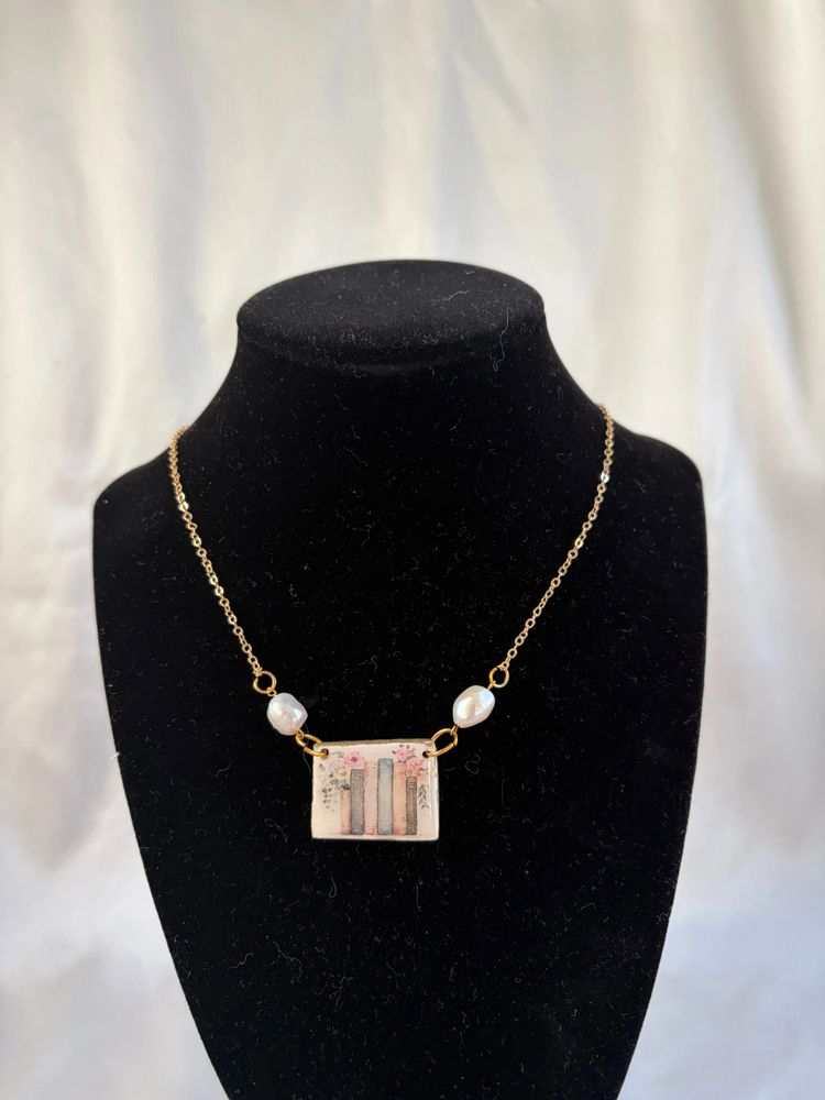 Delicate gold chain necklace with a book-themed pendant and pearl accents.